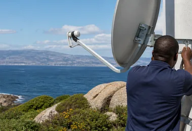 An accredited technician carrying a satellite dish up a Simon's Town garden path